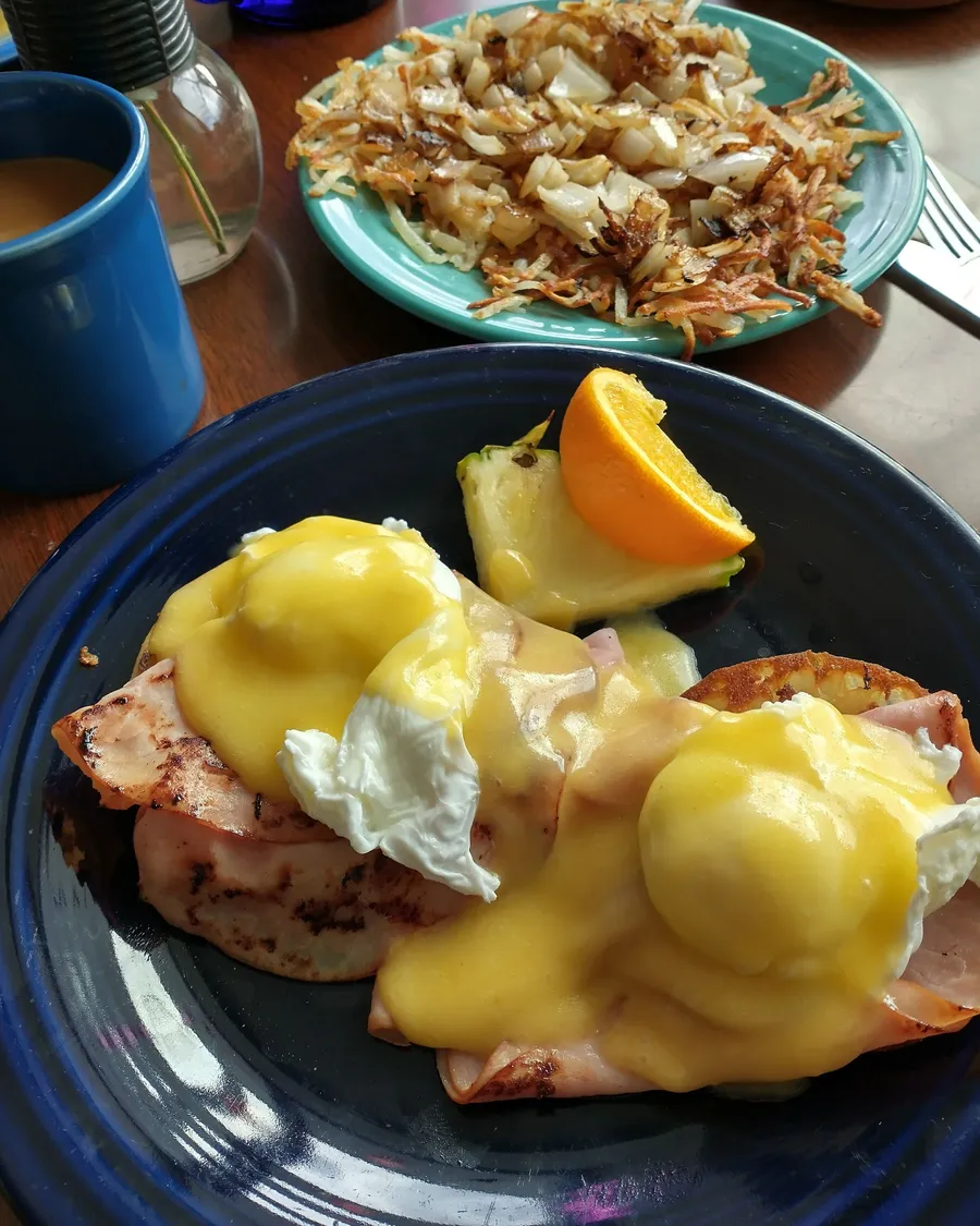 Eggs Benedict with scratch hollandaise and shaved ham on a blue Fiestaware plate, hash browns behind