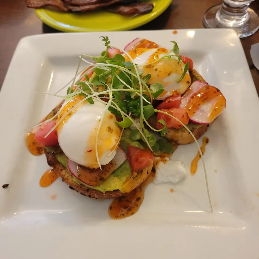 Avocado toast with two poached eggs, tomato, radish and microgreens under a hot-honey drizzle.