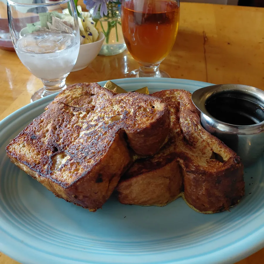 Thick-cut cinnamon French toast grilled golden, served beside iced tea and fresh flowers.