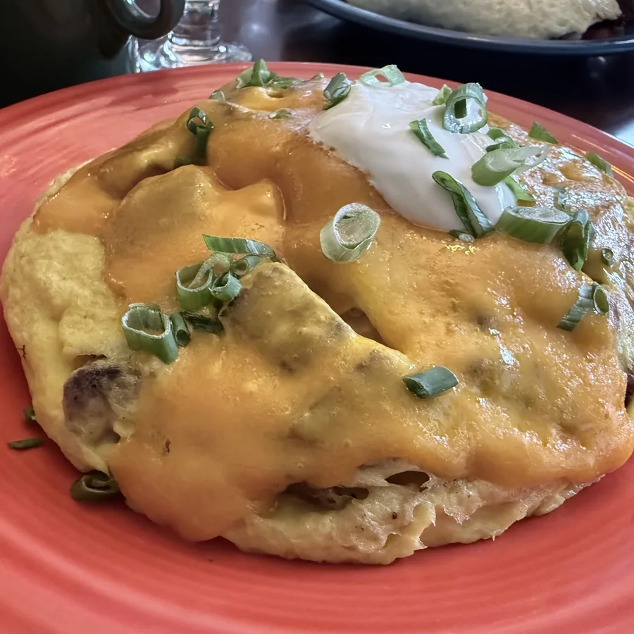 A cheddar omelette with sour cream and scallions on a coral Fiesta plate.