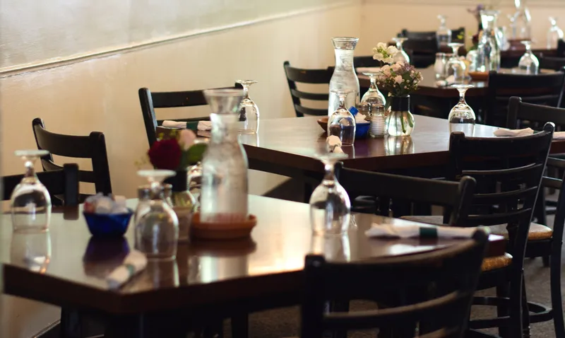 Dining room tables set with water carafes, fresh flowers and ladder-back chairs
