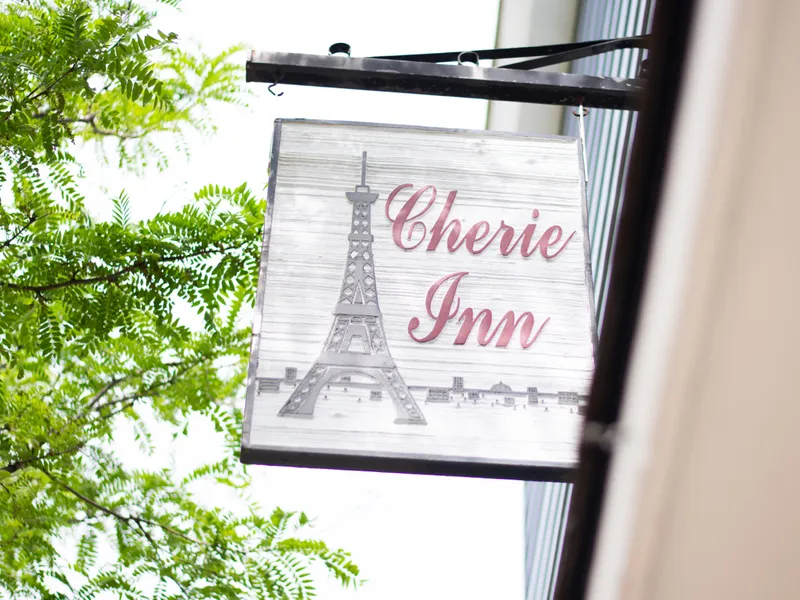 Cherie Inn’s whitewashed hanging sign with rose script and a pewter Eiffel Tower